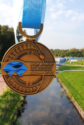 Duży, okrągły medal z Półmaratonu w Gdyni na tle rzeki Czarna Hańcza